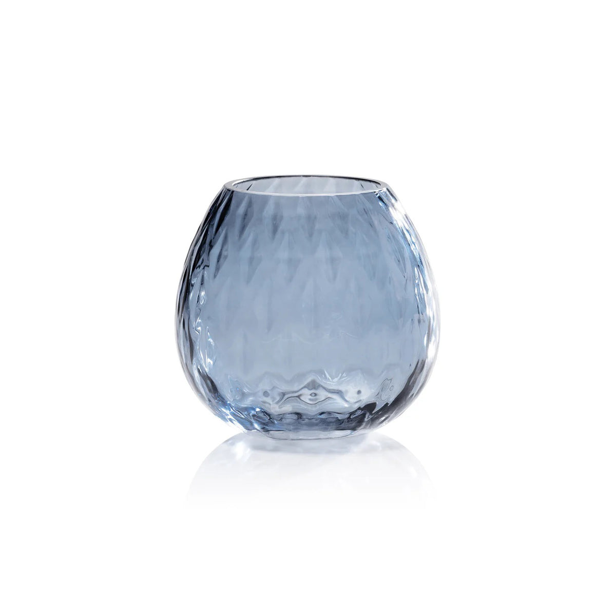 Three PRISM Multipurpose Optic Vase Candleholders by ZODAX in Deep Water Blue textured soda-lime glass, each approx. 4”, hold tealights; two in a woven tray, one on a blue book.