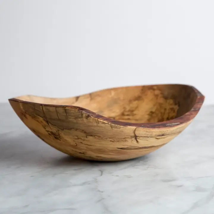 The SPENCER PETERMAN Spalted Oval Bowl with Live Edge 18" by PETERMANS BOARDS & BOWLS INC. is a handcrafted wooden piece created from spalted maple wood, featuring organic, curved edges. It rests on a smooth, gray surface. The bowl showcases a natural wood grain pattern in various shades of brown and beige, contributing to its rustic charm. Handcrafted in New England, the background is plain and light-colored.