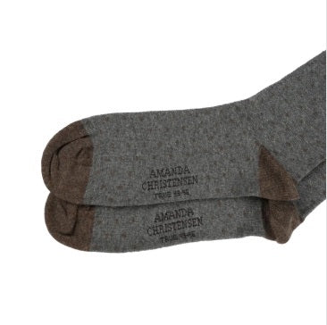 A pair of AMANDA CHRISTENSEN - TRUE DOT MID-CALF SOCKS IN GREY MELANGE, featuring contrasting brown heels, toes, and cuffs, crafted from a combed cotton blend and displayed flat on a white background. Some text is visible on the bottom of these Italian-made AMANDA CHRISTENSEN socks.