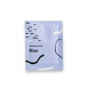 A person in a gray sleeve holds a "CORNEACARE - RISE EYELID WIPES" package, removing a white textured cloth infused with tea tree oil. In the background, there's a white shelf and sheer curtains, hinting at an eyelid care routine.