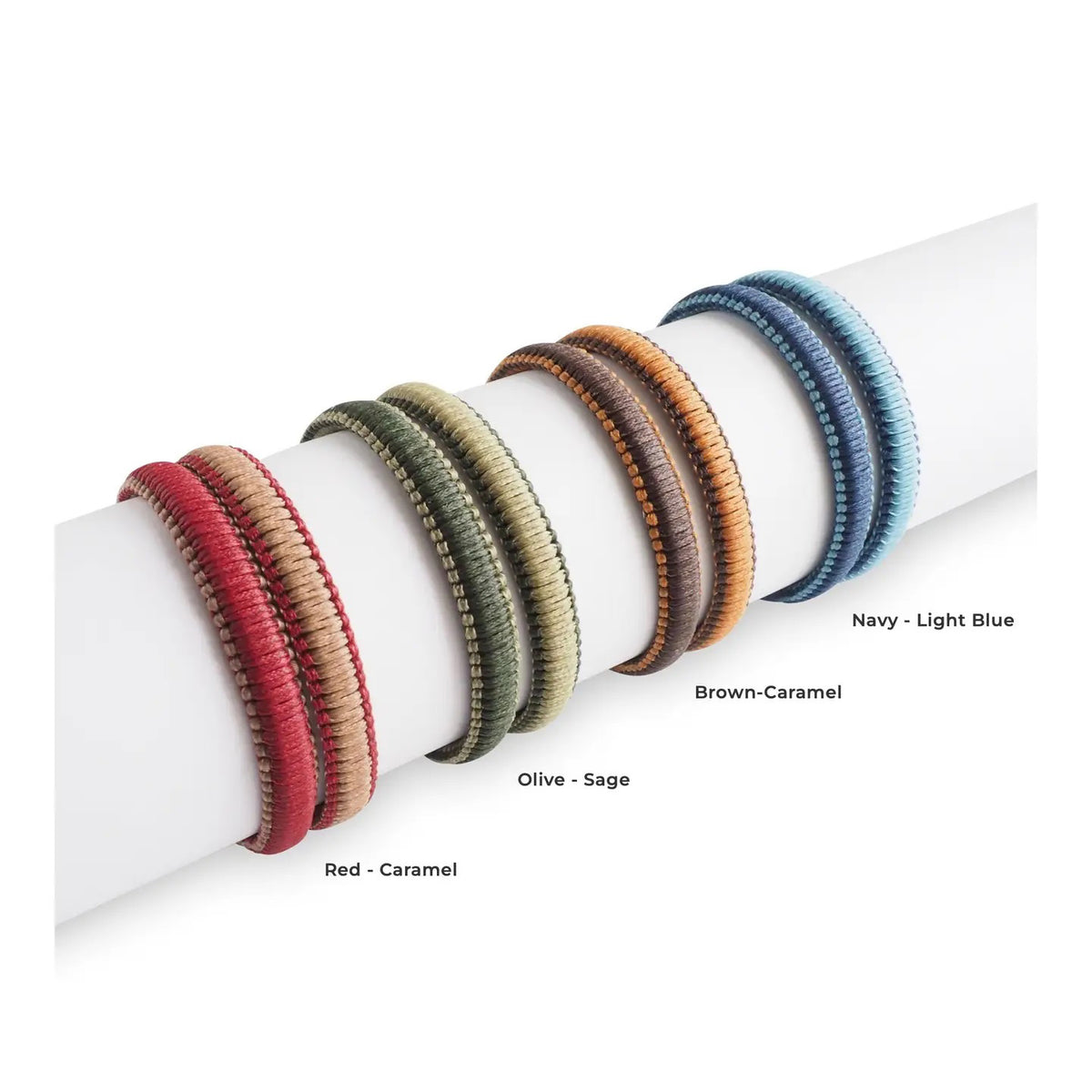 A close-up of a person’s hand resting on their chin, wearing two MAKARLA MEN'S REVERSIBLE SURFER BRACELETS in light blue and navy, paired with a light knit sweater.