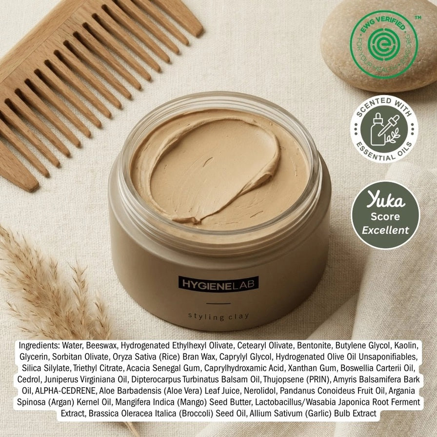 An open, round container of HYGIENELAB - STYLING CLAY displays the smooth, light gray clay inside with a swirled surface. This styling clay from HYGIENELAB provides a medium-strong hold and a natural matte finish.