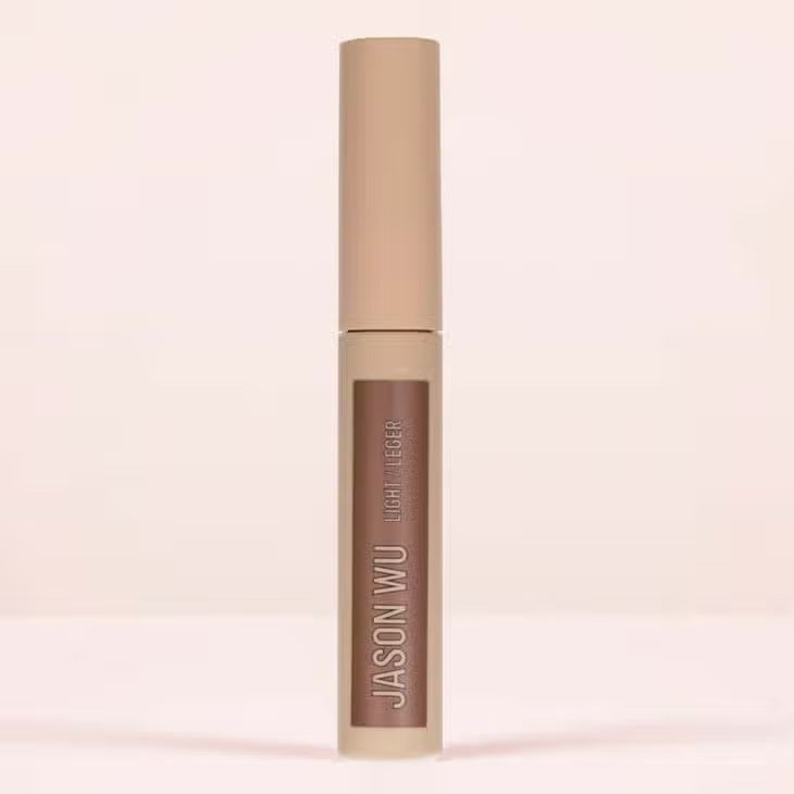 A cylindrical makeup product labeled &quot;FREE DA BROW LIGHT 2&quot; by JASON WU BEAUTY in white text against a beige background. The container features a matte finish and a beige cap, designed to help you define your brows effortlessly. Set against a neutral, light-colored background, the image captures its sleek elegance.
