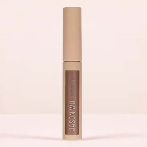 A cylindrical makeup product labeled "FREE DA BROW LIGHT 2" by JASON WU BEAUTY in white text against a beige background. The container features a matte finish and a beige cap, designed to help you define your brows effortlessly. Set against a neutral, light-colored background, the image captures its sleek elegance.