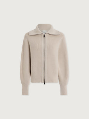A person wearing a dark brown VARLEY - ENRICO ZIP-THROUGH KNIT JACKET featuring a ribbed soft viscose knit, a high collar, and a front zipper, ideal for cool weather layering.
