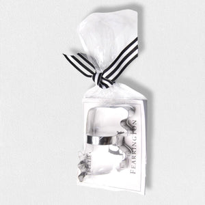 A cookie cutter from the FEARRINGTON SIGNATURE COLLECTION - BELTIE COOKIE CUTTER by AD RESOURCES is shaped like a cowboy boot, wrapped in clear plastic and tied with a black and white striped ribbon. Attached is a tag with the word "FEARINGTON," an image of the cookie cutter, and a recipe card for Beltie Cow cookies.