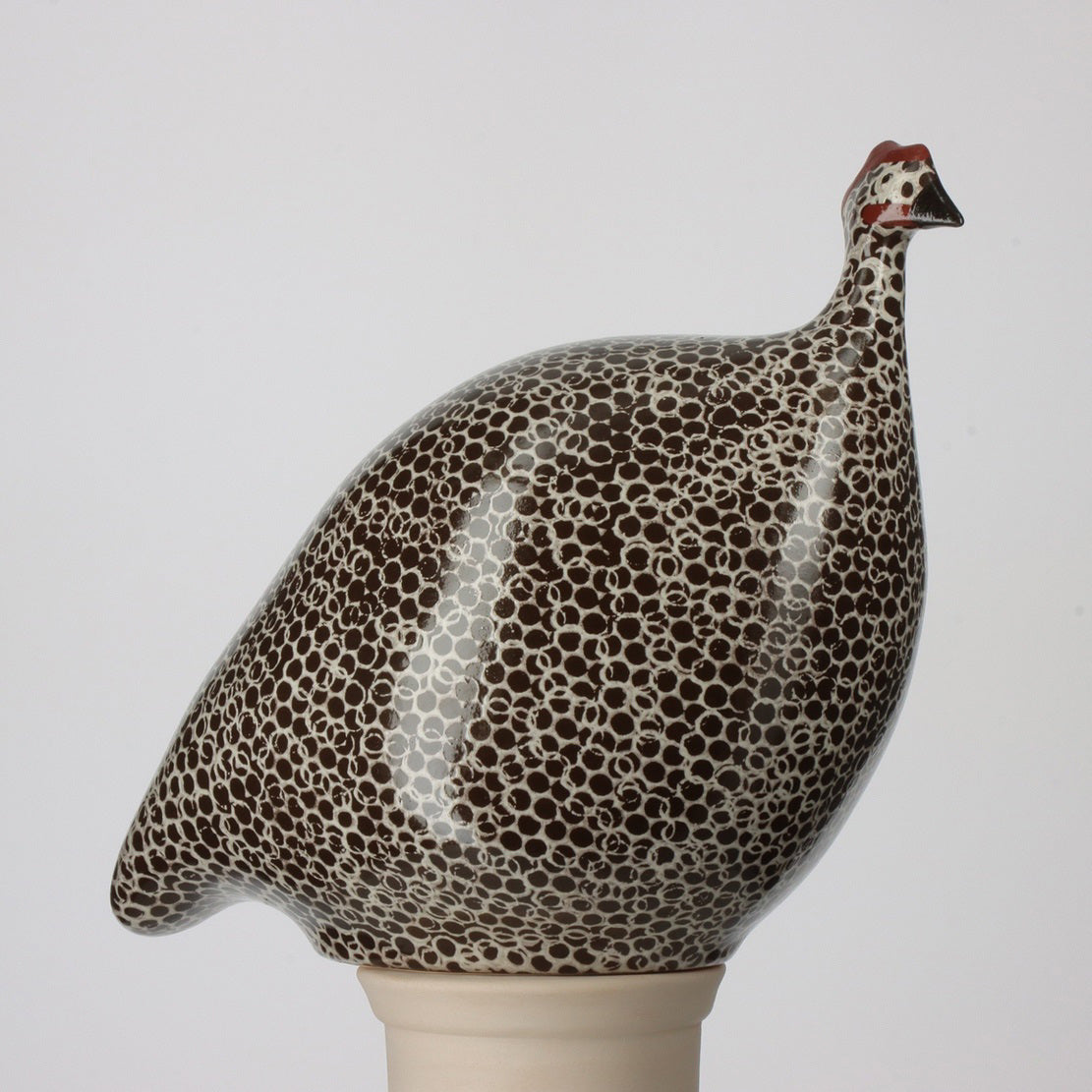 Illustration featuring three bird figurines reminiscent of French guinea hens in white, gray, and black, labeled by size: large (24 cm), medium (20 cm), and small (17 cm). On the right stands a black mug with "MUG" inscribed, measuring 8.5 cm in height. The backdrop is gray, enhancing the ceramic sculptures from LES CERAMIQUES DE LUSSAN, including the medium ceramic French guinea in black spotted white.