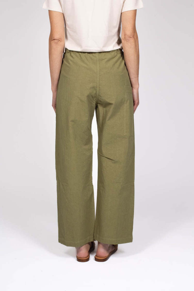 Against a plain background, a person wears THE LITTLE PROJECT&#39;s AMBER PANT in olive-green, made from Japanese cotton with a drawstring waist. They&#39;re styled with a white short-sleeve top and brown woven flat sandals. These versatile pants are already becoming a best seller.