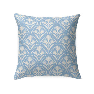 A wicker chair with a white cushion and a LOOM AND CLOTH - SERENA TAILORED PILLOW by LOOM & CLOTH sits next to a white nightstand with two vases, set against a wall featuring blue and white patterned wallpaper.