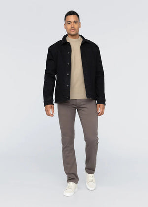 A person faces forward against a plain light background, wearing a black jacket over a beige sweater, DUER No Sweat Straight Pants in Canteen, and white sneakers.
