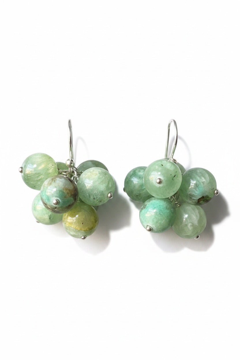 The ANN LIGHTFOOT - AZURITE JADE CLUSTER EARRINGS by ANN LIGHTFOOT feature clusters of round, green azurite jade gemstones in varying shades, suspended from sterling silver hooks and displayed on a black rod against a plain white background.
