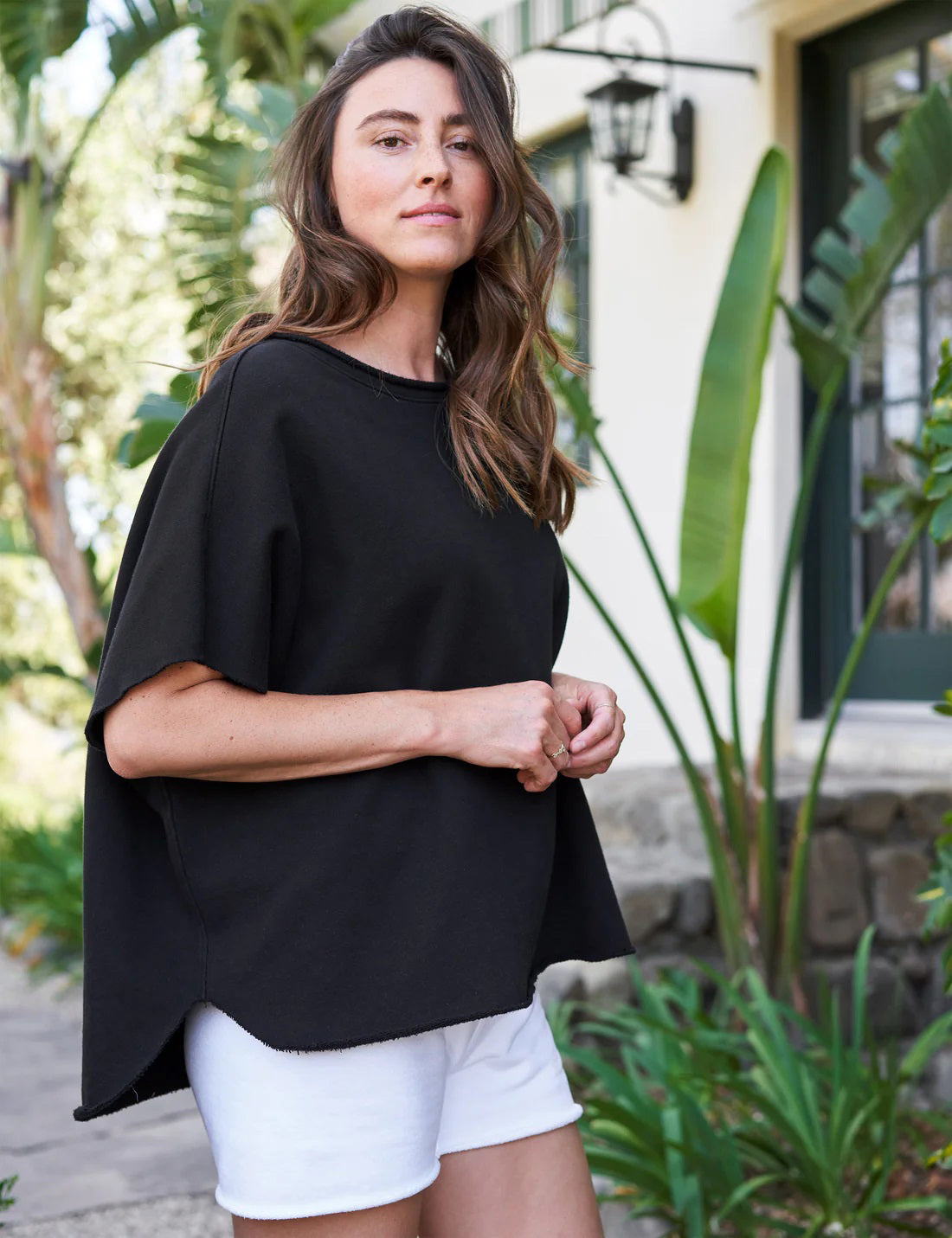 The FRANK &amp; EILEEN OLIVE ORIGINAL CAPELET in black, by FRANK &amp; EILEEN, is a black oversized T-shirt with a round neckline and short, wide sleeves. Made from 100% cotton, it features a loose fit and simple design reminiscent of a capelet against a light textured background.