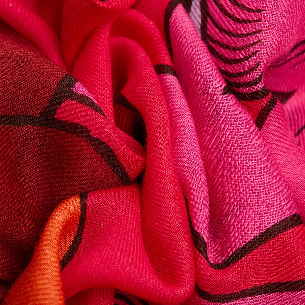 Close-up of the INOUI EDITIONS - CAVALE WOOL SCARF IN RED by INOUI, featuring crumpled wool in red, pink, and orange with dark brown abstract lines. Its woven texture and bold style make it a perfect winter accessory.