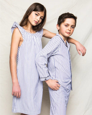 The PETITE PLUME FEARRINGTON LIFESTYLE COLLECTION - CHILDREN'S TWILL NAVY FRENCH TICKING PAJAMA SET is a delightful option for kids, featuring long sleeves and pants with chic vertical white and gray stripes. This set is crafted from yarn-dyed cotton, boasting a top with a collar, full button-down front, and a single chest pocket adorned with matching fabric piping along the cuffs and pocket opening.