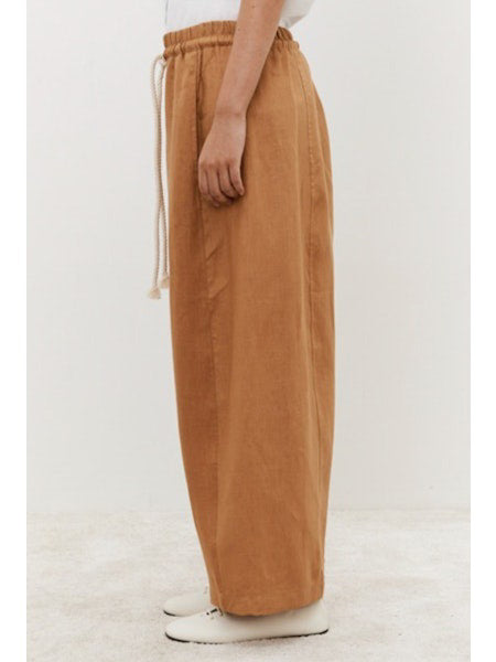 A person in MEIMEIJ Linen Drawstring Pants, featuring a relaxed wide-leg brown silhouette with a white drawstring, pairs them with white shoes against a plain light background, showcasing their adjustable fit for a casual look.