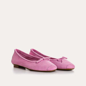 A close-up of the REQINS - HARMONY SUEDE BALLERINA FLATS IN PINK, featuring a bow detail on the front, photographed on a light surface—an elegant update to this classic women’s shoe by REQINS.