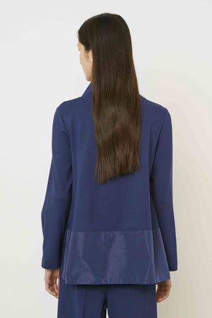 A woman with long brown hair, seen from behind, wears the MEIMEIJ Mixed Media Cowl Neck Top in dark blue with a shiny panel at the bottom and matching pants. She stands against a plain, light background.