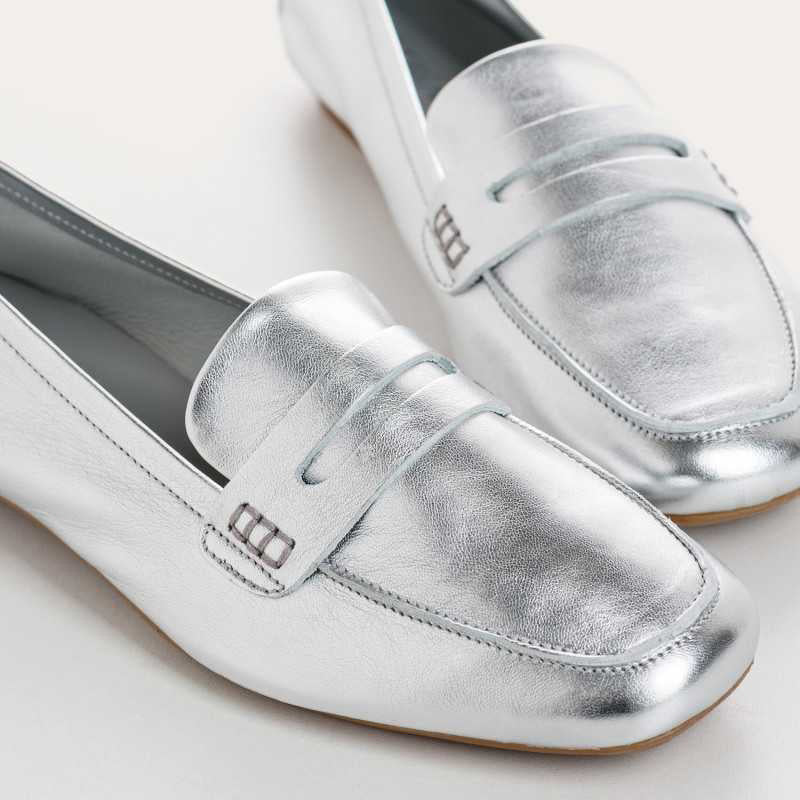 The REQINS - HEMA METALLIC LOAFER IN SILVER is a shimmering leather loafer with a low heel and classic penny slot detail, displayed in side profile against a plain light background.