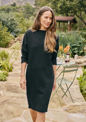 The FRANK & EILEEN - IZZIE SWEATSHIRT PARTY DRESS, crafted from 100% cotton, is laid flat against a white textured background. This simple black dress showcases long sleeves, a crew neckline, and a straight silhouette extending to knee-length.