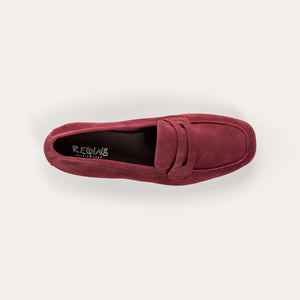 Close-up of the REQINS - HEMA SUEDE LOAFER IN BORDEAUX by REQINS, showcasing artisanal craftsmanship with burgundy suede, detailed stitching, a front strap, and a soft leather insole, displayed on a light surface.