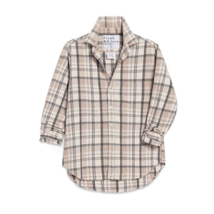 A woman smiles with her eyes closed, wearing the FRANK & EILEEN EILEEN Relaxed Button Up Shirt in Italian Flannel Cream Sand Grey Plaid, paired with light gray sweatpants in a cozy room by a fireplace, with candles and books in the background.