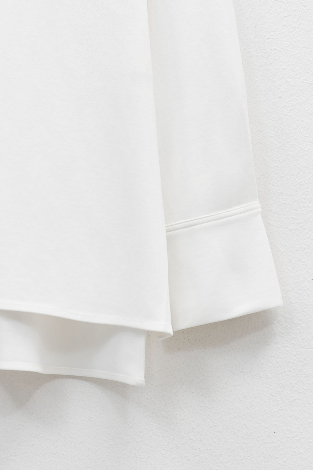 The ELEH - THE BIANCA CUFF TOP by ELEH is a plain white, long-sleeve crew neck shirt with wide sleeves, a loose fit, and an extended back hem for effortless style. Displayed against a white background, this versatile piece features a minimalist silhouette.