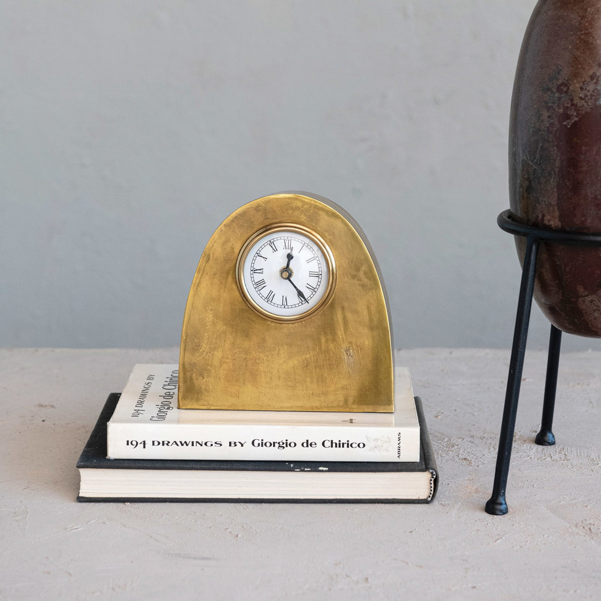 The CREATIVE COOP ARCHED METAL MANTEL CLOCK features an antique gold finish, a rounded top, and Roman numerals on a white face, shown against a plain white background.