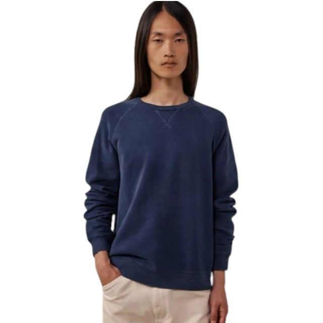 A person with long, straight hair is wearing the HARTFORD - LIGHT FLEECE SWEATSHIRT IN NAVY by HARTFORD and light-colored pants, standing with one hand in their pocket against a plain white background.