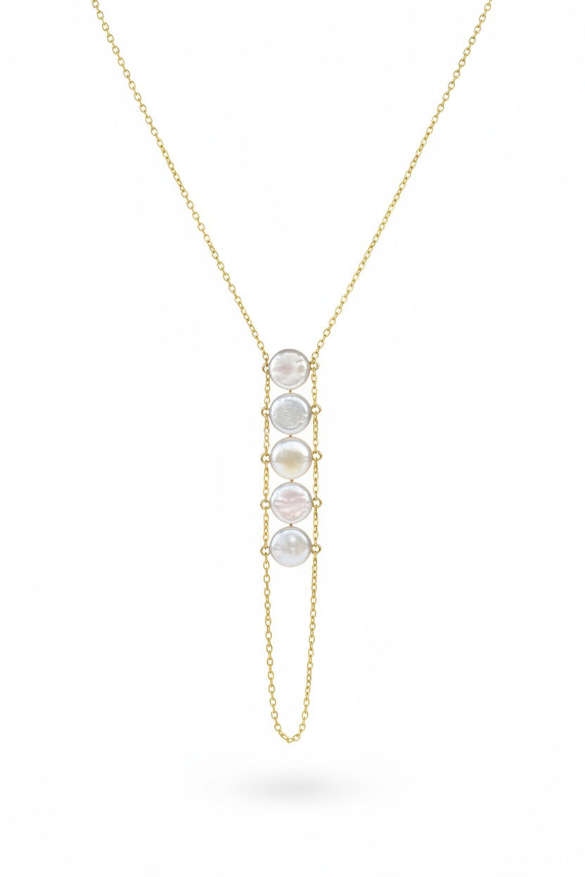 A woman in a beige top wears the GOLDISH - LADDERS TO BLISS PEARL NECKLACE, featuring round white stones, as she poses with crossed arms and a turned head, embodying balance and harmony.