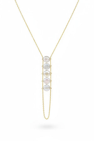 A woman in a beige top wears the GOLDISH - LADDERS TO BLISS PEARL NECKLACE, featuring round white stones, as she poses with crossed arms and a turned head, embodying balance and harmony.
