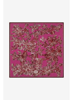 A woman with straight black hair wears a cream sweater and the INOUI EDITIONS - ARBORI Square Wool Scarf in Fuschia by INOUI, crafted from 100% wool and featuring a leaf pattern, draped around her neck against a plain light background.