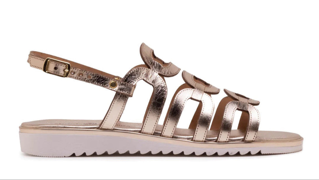 A metallic gold flat sandal with a white ridged sole, open toe, cut-out arch design, and an adjustable ankle strap with a buckle.