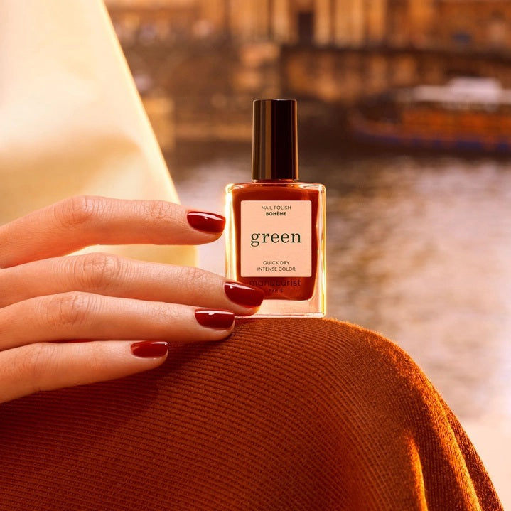 A close-up of MANUCURIST - GREEN™ NAIL POLISH IN BOHEMIAN by MANUCURIST INC being smoothly applied with a brush, revealing its glossy, reflective red finish and visible bristle strokes.