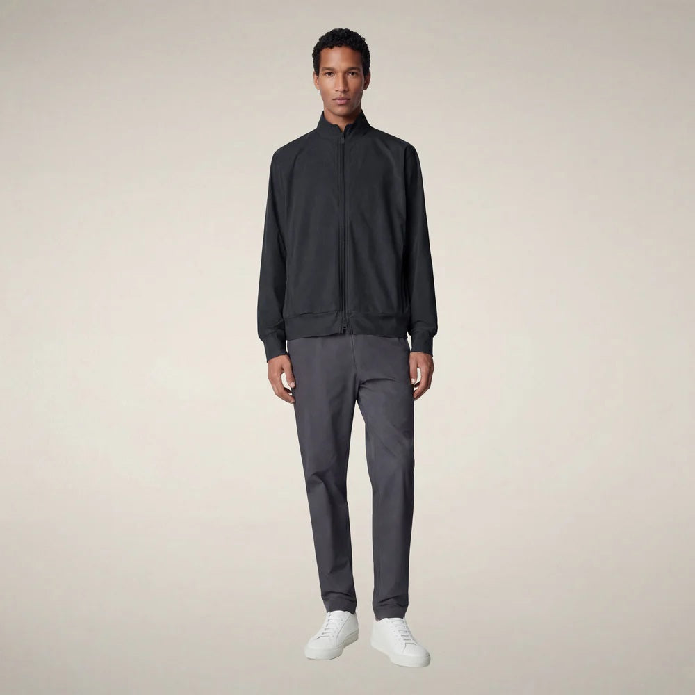 A person stands facing forward, wearing the SAVE THE DUCK - TULIO JACKET IN BLUE BLACK by SAVE THE DUCK, paired with gray pants and white sneakers, against a plain light background.