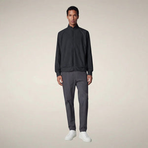 A person stands facing forward, wearing the SAVE THE DUCK - TULIO JACKET IN BLUE BLACK by SAVE THE DUCK, paired with gray pants and white sneakers, against a plain light background.