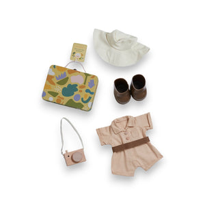 An OLLI ELLA USA DINKUM DOLL from the Pretend Pack Travel Sets, outfitted in a wide-brimmed hat, khaki overalls, and brown boots, poses with a petite suitcase. The backdrop showcases a vibrant, abstract pattern filled with diverse shapes and pastel hues, perfect for sparking endless imaginative adventures.