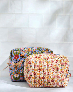 The PRINTFRESH Bee Tapestry Oversized Pouch Duo in Delphinium Blue features two quilted makeup pouches: the larger pouch showcases a blue bee and floral print, while the smaller pouch displays a cream background with red, yellow, and blue geometric shapes. Both PRINTFRESH bags are displayed on a tiled surface.