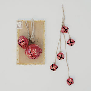 Creative Co-op JINGLE BELL ORNAMENT WITH SNOWFLAKES, a red spherical metal bell featuring gold snowflake designs, hanging from a rustic jute loop.