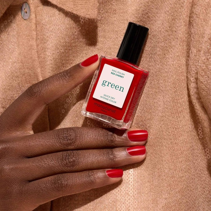 A close-up of the MANUCURIST - GREEN™ NAIL POLISH IN RED CHERRY brush, surrounded by glossy vegan polish from MANUCURIST INC, creating smooth ripples on the vibrant red surface.