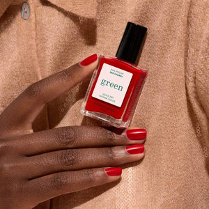 A close-up of the MANUCURIST - GREEN™ NAIL POLISH IN RED CHERRY brush, surrounded by glossy vegan polish from MANUCURIST INC, creating smooth ripples on the vibrant red surface.