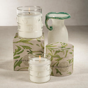The ZODAX GRAND CASABLANCA CANDLE - WILD TUBEROSE, 6.5OZ features white wax in a jar beside a round box with green leafy patterns, filling the air with wild tuberose—a beautiful botanical gift candle for any occasion.