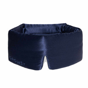 A person wearing a white tank top is lying on a pillow with the DROWSY - SATIN SLEEP MASK by DROWSY SLEEP CO covering their eyes. They look relaxed, enjoying beauty sleep as their hand rests gently on the pillow.