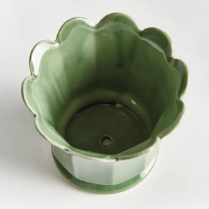 The NAPA HOME AND GARDEN - Maline Footed Pot in Green (Small) is a light green ceramic pot featuring scalloped edges and vertical panels, perched on a small round base, set against a plain white background.