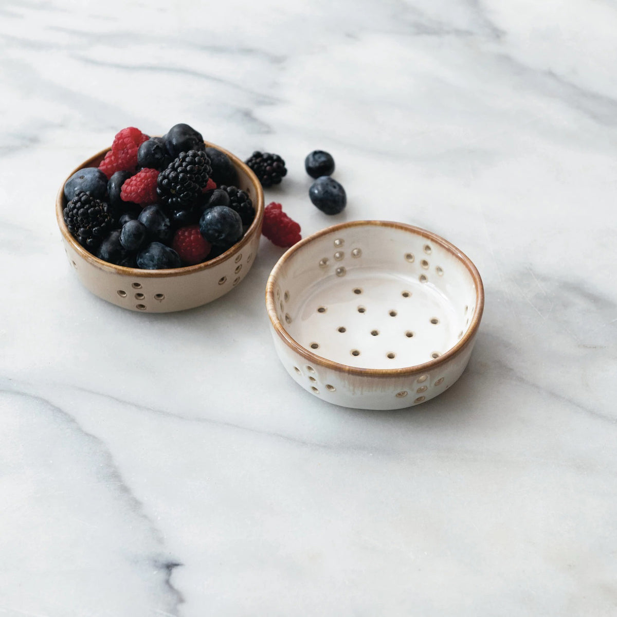 Four Creative Coop STONEWARE BERRY BOWLs, each measuring 4&quot; in diameter, are displayed against a white background. The two bowls on the left feature a white reactive glaze with brown rims, while the two on the right are entirely brown. Each pair includes both a top-down and side view of these ceramic colander bowls with holes.