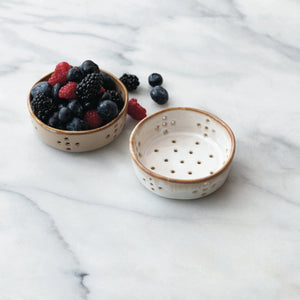 Set of four STONEWARE BERRY BOWLS by CREATIVE COOP—two white, two brown—each with multiple drainage holes and a smooth reactive glaze. Shown from top and side views on a white background.