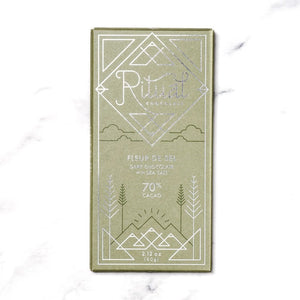 A green RITUAL CHOCOLATE - FLEUR DE SEL CHOCOLATE BAR 70% CACAO with silver geometric designs and text on the wrapper, shown on a white marble background.