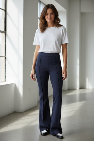 A woman models the SPANX Perfect Pant High Rise Flare in navy with a matching blazer, white fitted top, and black-and-white shoes, highlighting the sleek pull-on design from SPANX against a plain light background.
