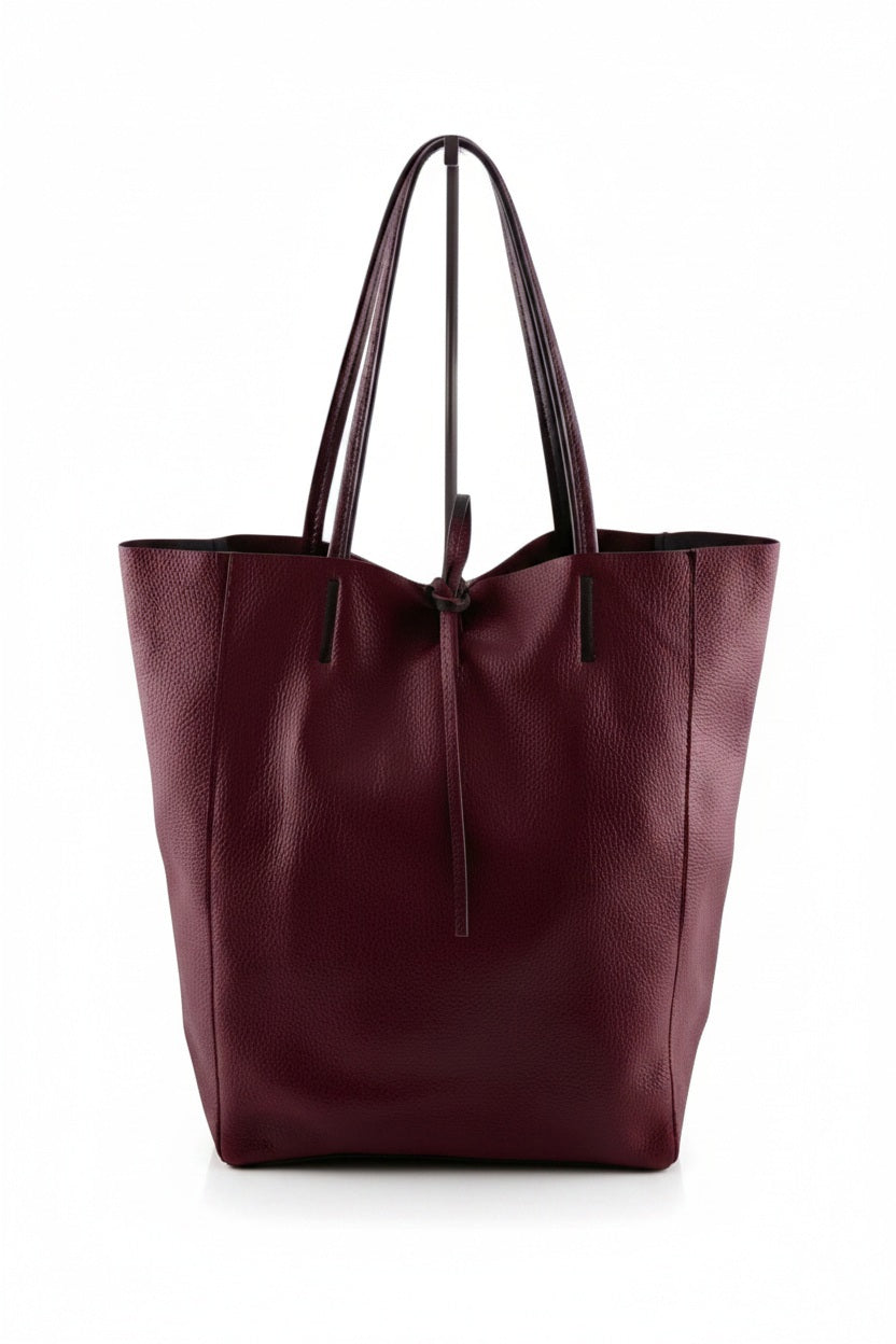 Introducing the LEATHER TOTE BAG IN DARK WINE by JIJOU CAPRI—a spacious Italian leather tote in a deep wine hue, designed with two strong handles and a convenient drawstring closure, ideal for carrying your daily essentials. Shown against a plain white background.
