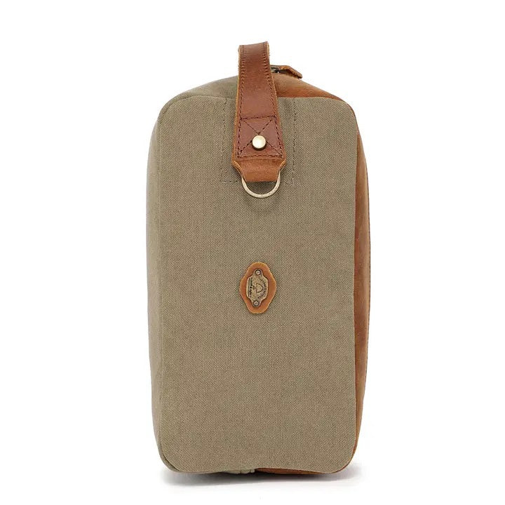 The TSD BRAND Valley Oak Toiletry Bag in olive is a rectangular, handcrafted travel essential made from durable canvas, featuring a tan leather strap and a small leather patch for added style.