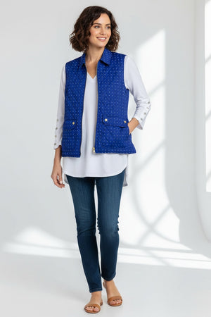 A woman wears the HINSON WU - LAUREN REVERSIBLE VEST, featuring blue quilted cotton with white polka dots and a gold-tone zipper, over a white long-sleeve shirt and dark jeans, standing against a plain light background.